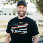 Smiling bearded man in Grand View Roofing shirt and baseball cap outdoors