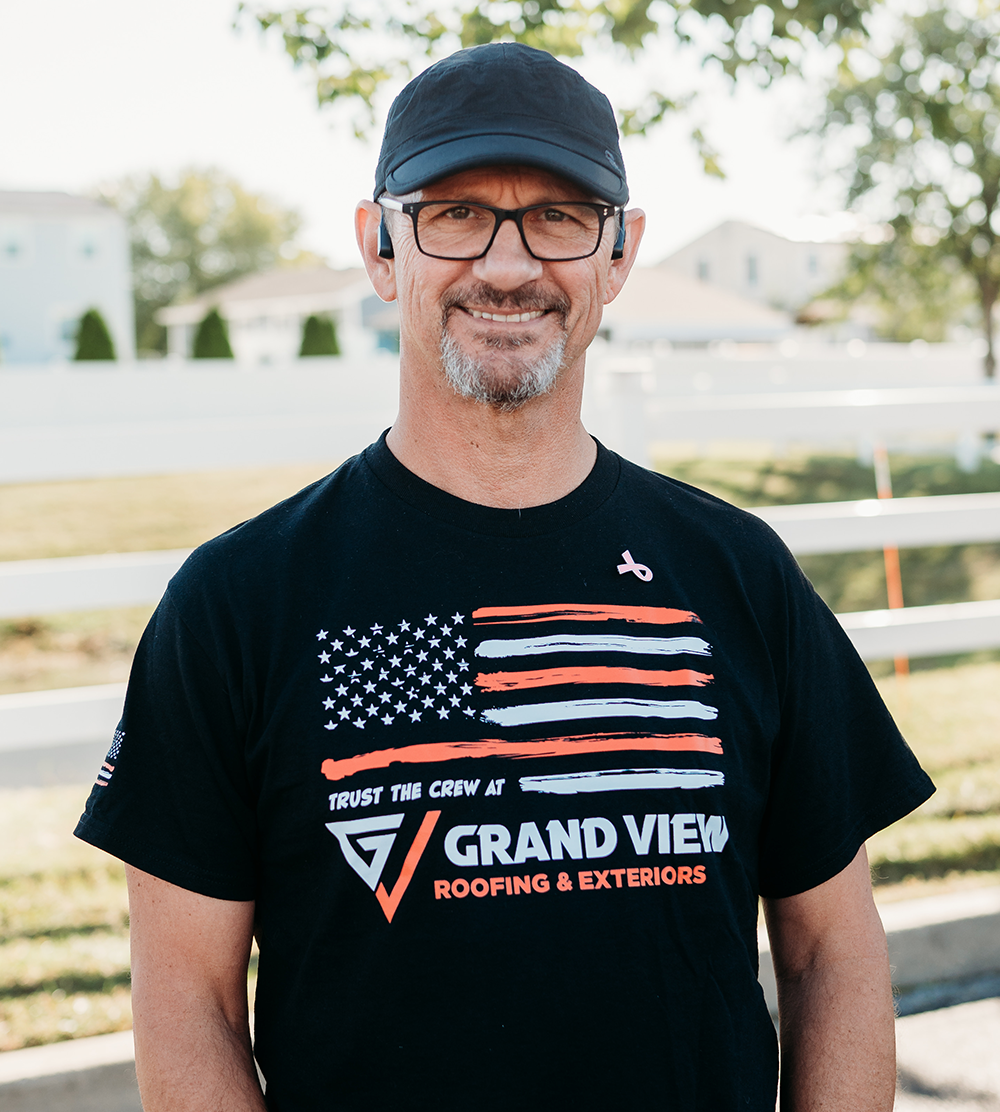Smiling man in black cap and glasses wearing Grand View Roofing company shirt