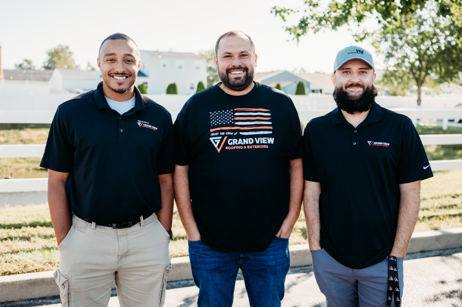 Three Grand View Roofing & Exteriors team members smiling outdoors in company shirts