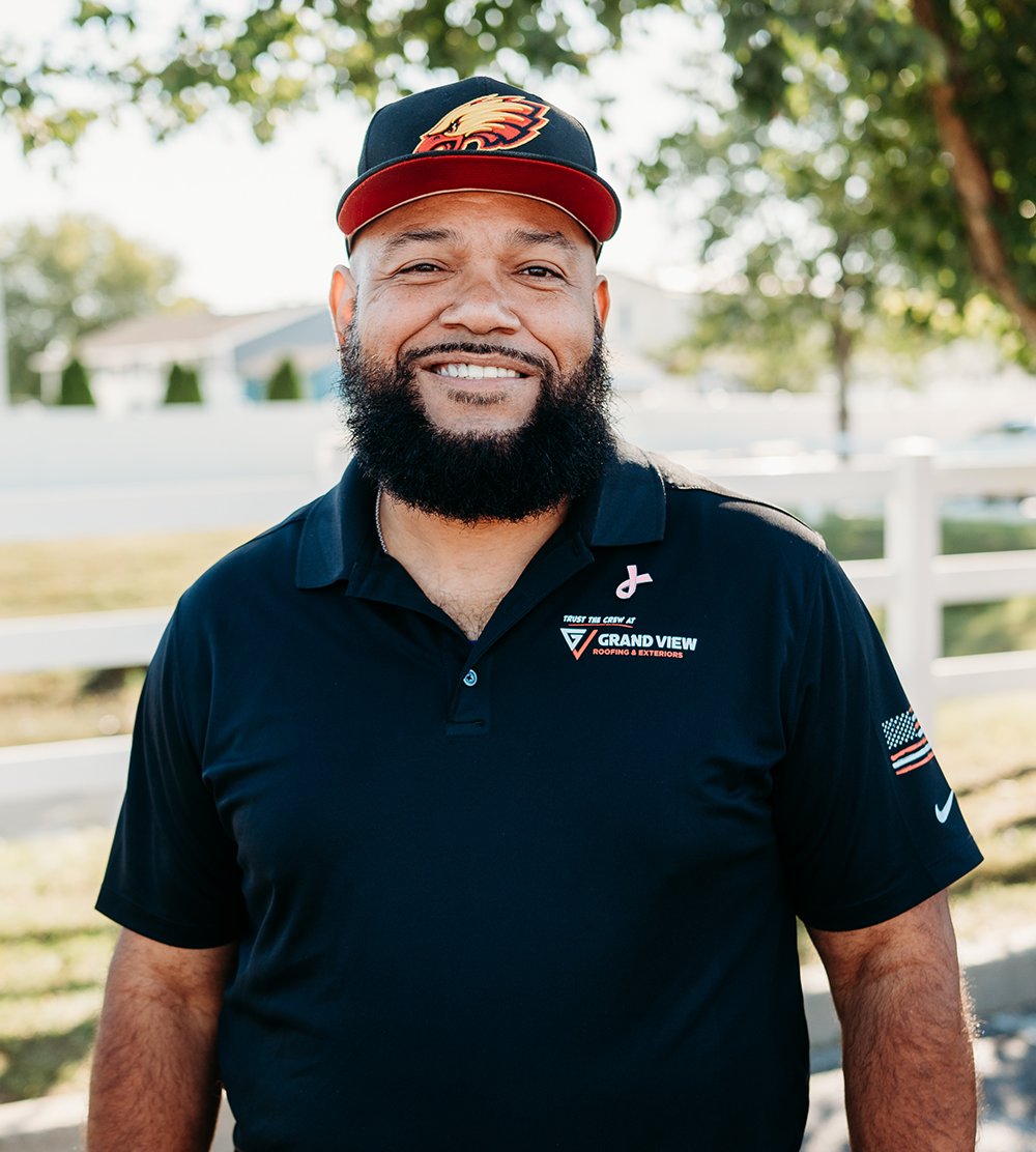 Smiling bearded man in Grand View Roofing polo shirt and baseball cap outdoors