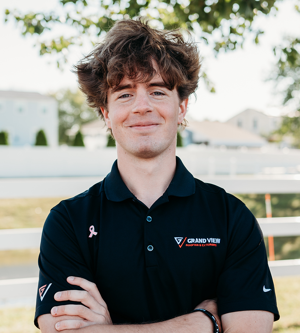 Young man with curly brown hair smiling in black Grand View Roofing polo shirt