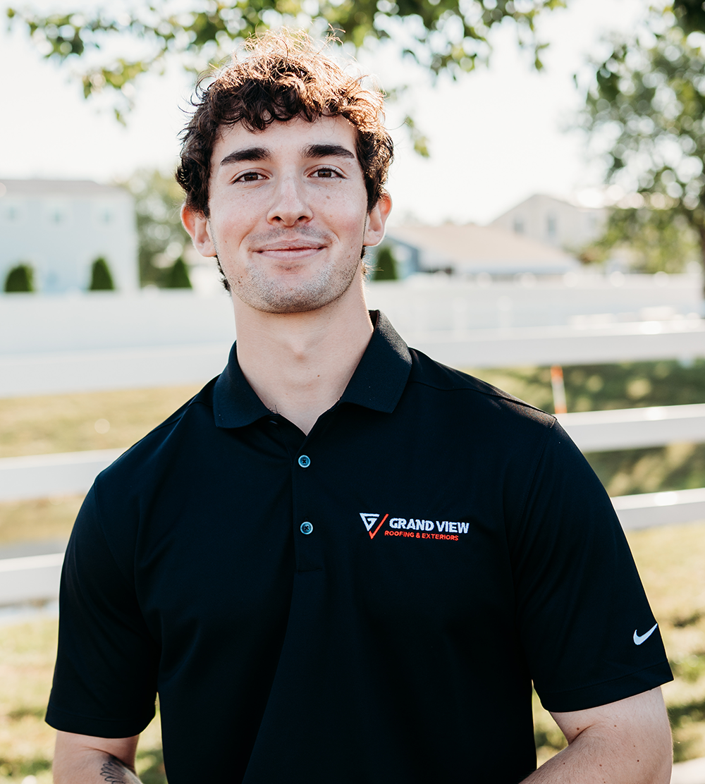 Young man with curly hair smiling in black Grand View Roofing polo shirt outdoors