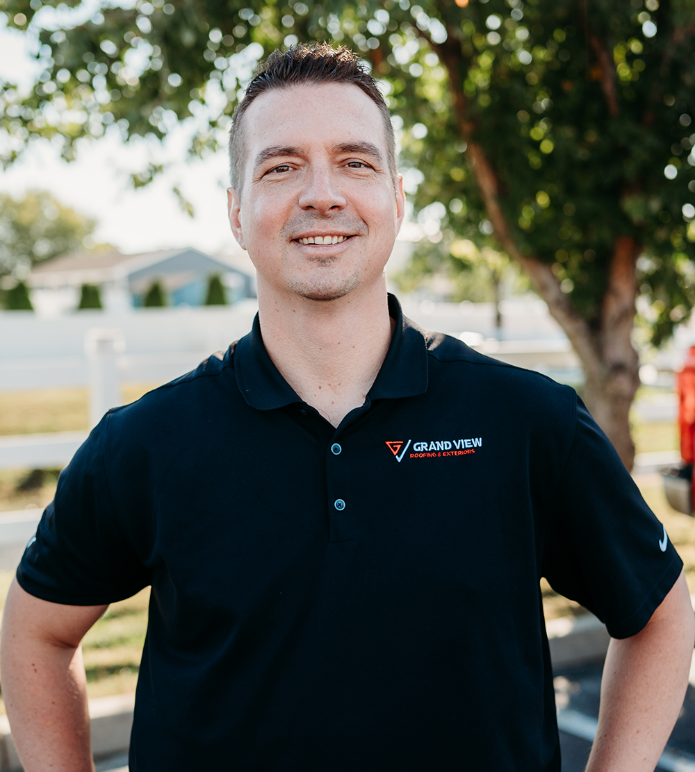 Professional man in navy Grand View Roofing & Exteriors polo shirt smiling outdoors