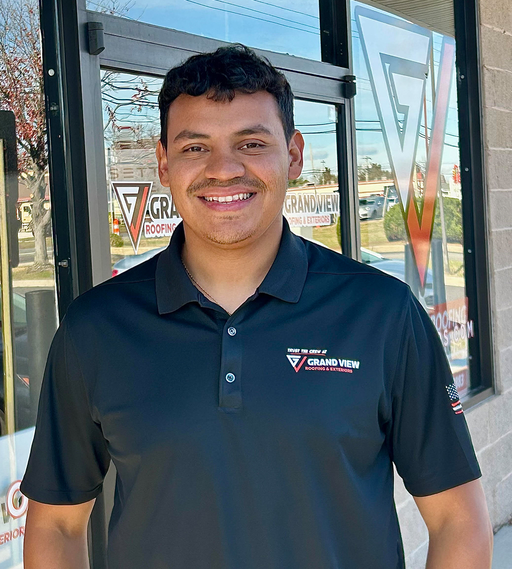 Smiling man in navy Grand View Roofing polo shirt standing outside office