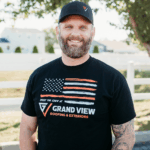 Smiling bearded man in Grand View Roofing shirt and baseball cap outdoors