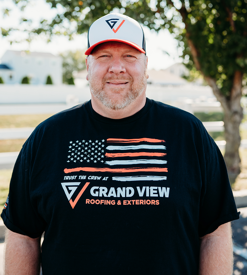 Smiling man in Grand View Roofing branded shirt and cap with American flag design