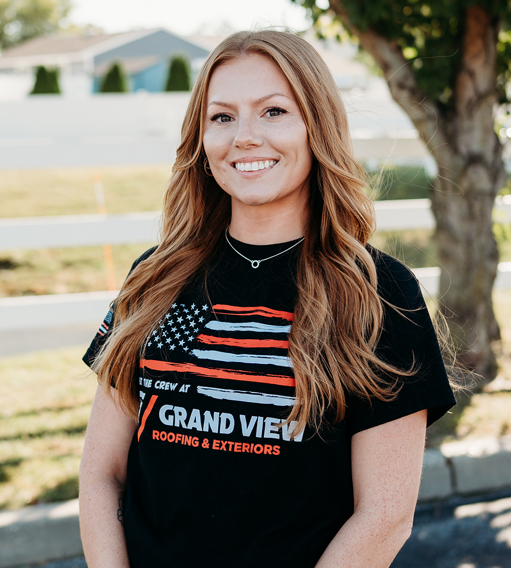 Smiling woman with long blonde hair wearing Grand View Roofing & Exteriors t-shirt