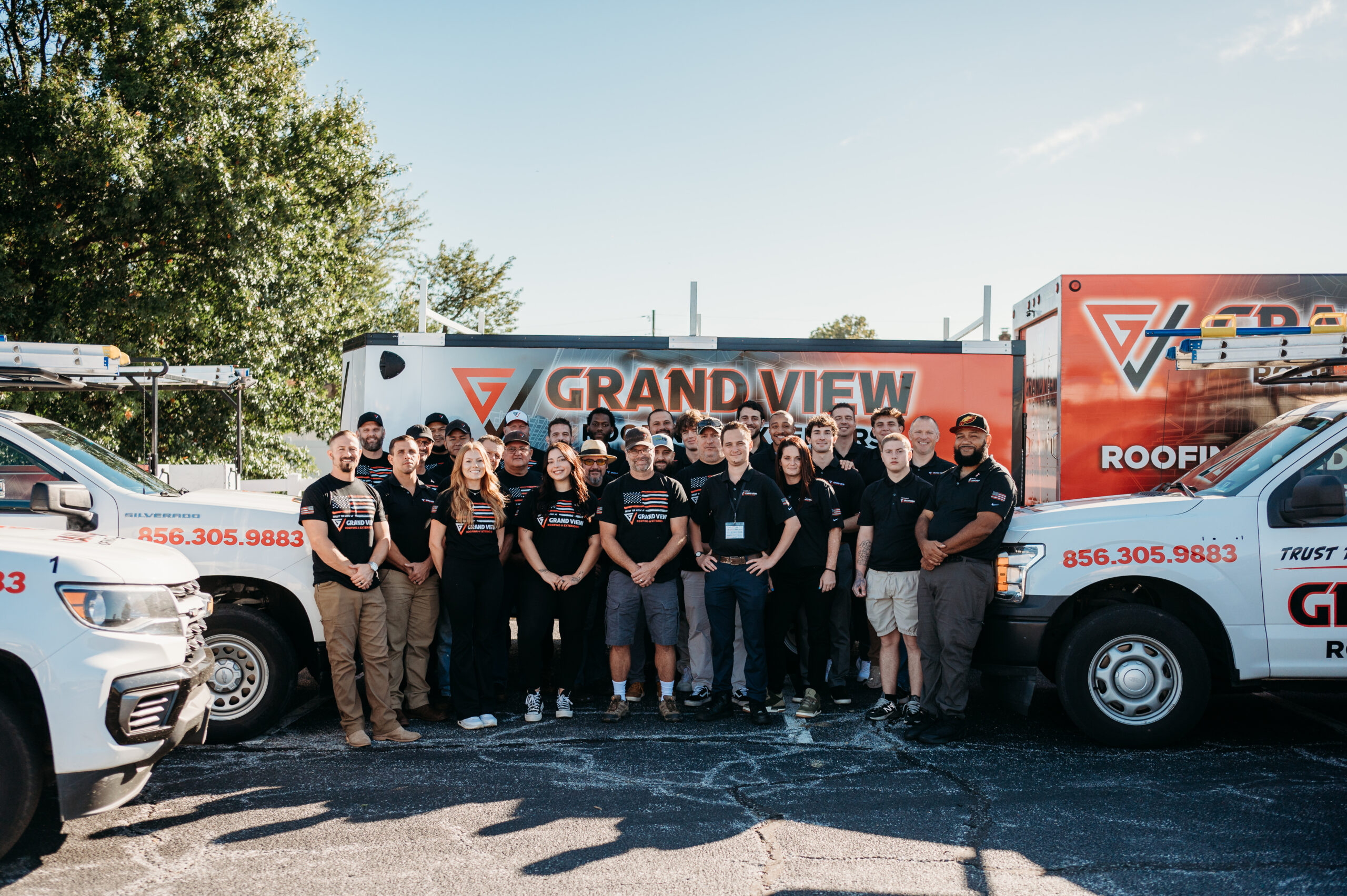 Grand View Roofing team group photo with company trucks and branded trailer
