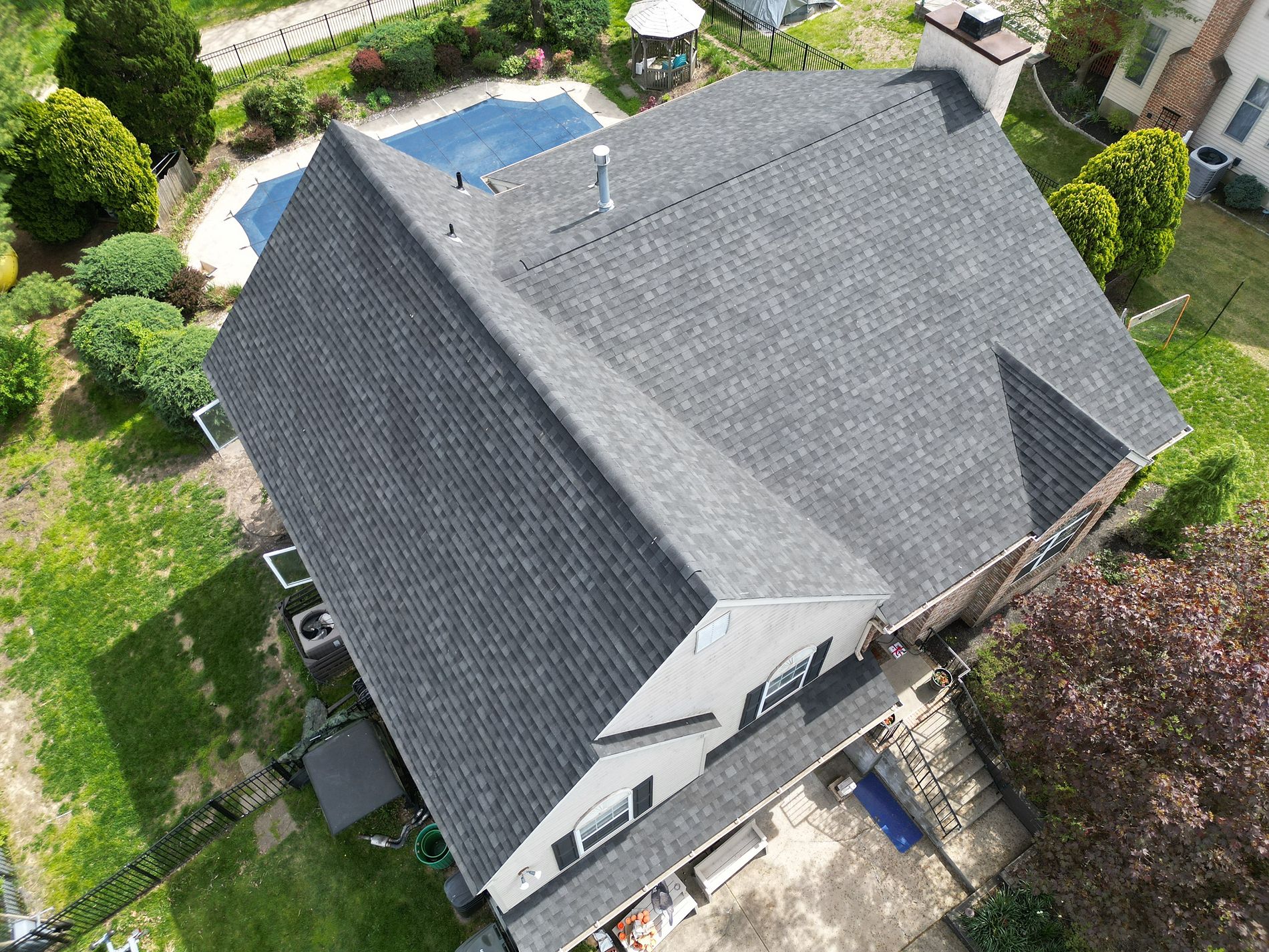 Aerial view of a house with a new gray shingle roof and surrounding greenery.