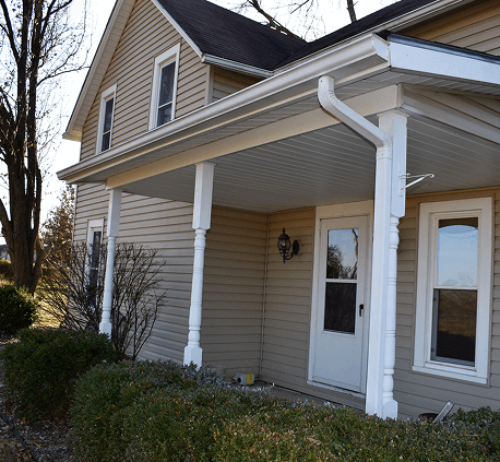 Suburban house with a porch and beige siding under sunny sky