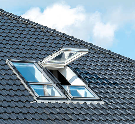 Modern skylight window open on a black tiled roof under blue sky.