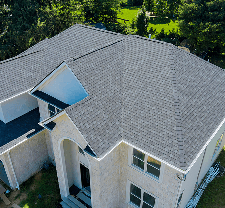 Aerial view of a modern house with a new shingle roof and surrounding greenery.